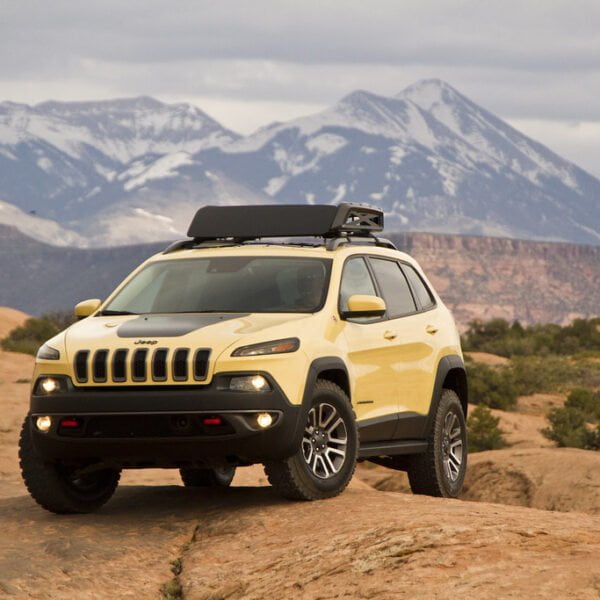 A Jeep SUV parked on rocky terrain with snow-capped mountains in the background.