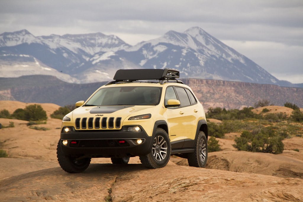 A Jeep SUV parked on rocky terrain with snow-capped mountains in the background.