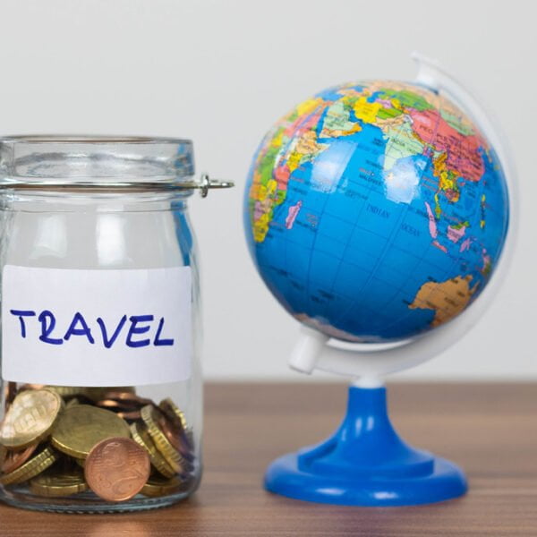 A clear glass jar filled with coins labeled "TRAVEL" next to a small globe on a wooden surface.