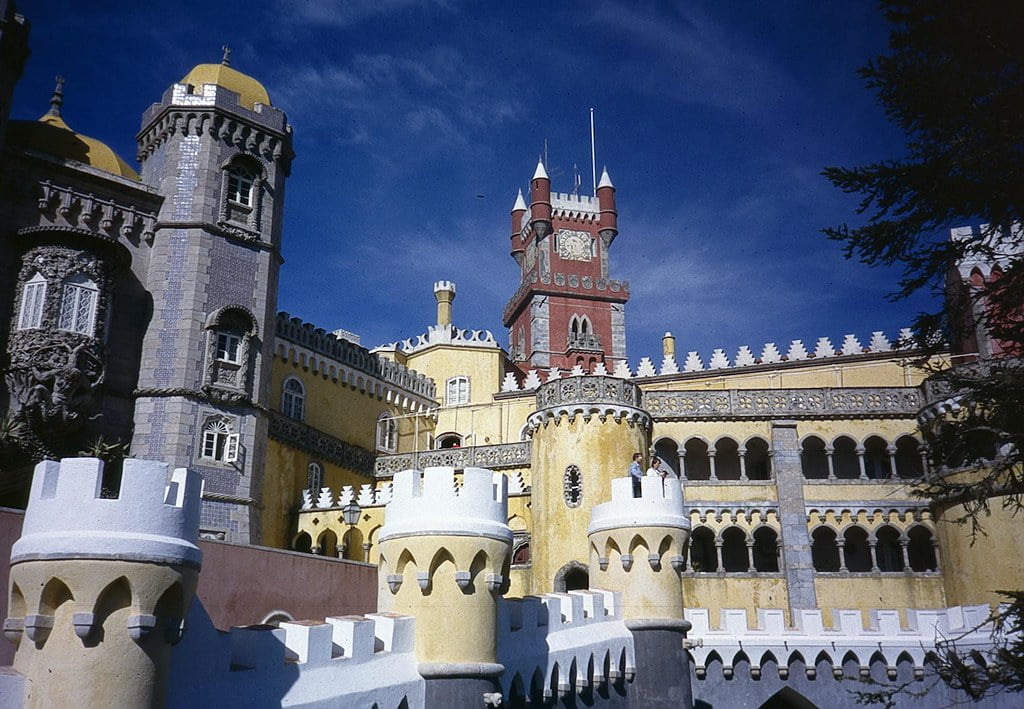 Exterior view of the colorful Pena Palace with its red and yellow walls, ornate architectural details, and a clear blue sky in the background.