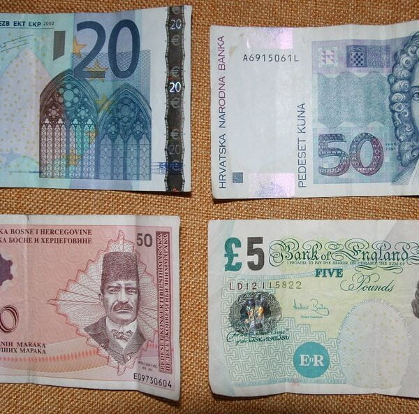 Four different banknotes are spread out on a surface: a 20 Euro note, a 50 Croatian Kuna, a 50 Bosnia and Herzegovina Convertible Marks, and a 5 British Pound sterling.
