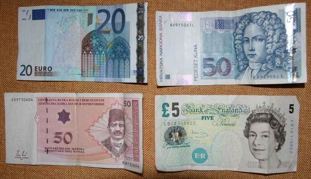 Four different banknotes are spread out on a surface: a 20 Euro note, a 50 Croatian Kuna, a 50 Bosnia and Herzegovina Convertible Marks, and a 5 British Pound sterling.