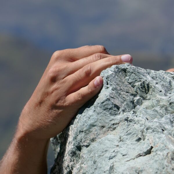 Close-up of a person's hand gripping a rocky surface with a blurry background that suggests a high-altitude location.
