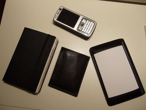 A notebook, a wallet, a flip cellphone, and a digital tablet laid out on a table.