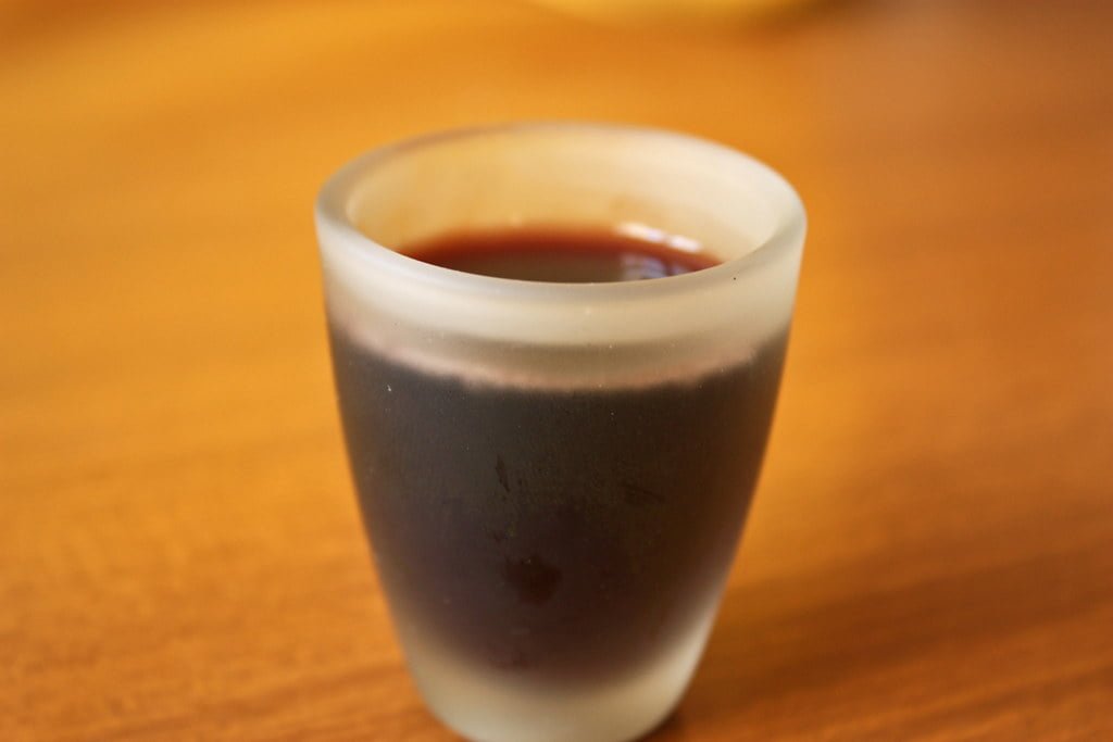 A frosted glass cup filled with a dark liquid on a wooden surface.
