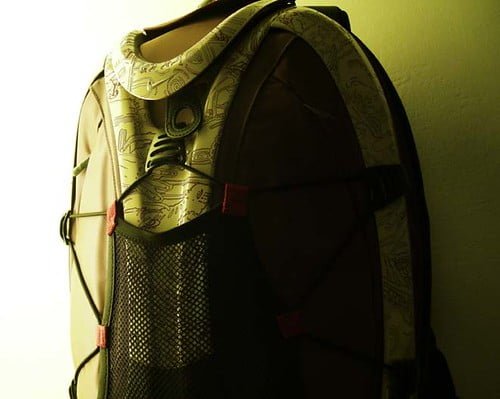 A backpack with a patterned design and a mesh side pocket, highlighted by soft lighting against a dark background.