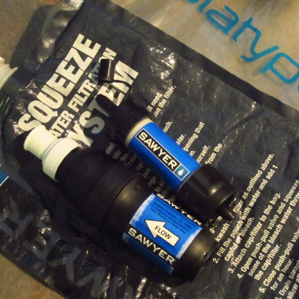 A Sawyer Squeeze water filtration system and a Platypus water bag laid out on a flat surface.