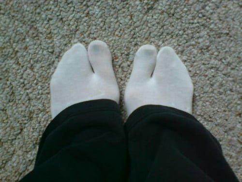 A person standing on a textured surface wearing white toe socks and black pants.