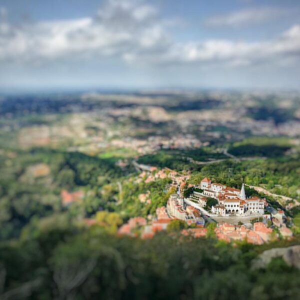 Aerial view of a white historical building complex with red roofs surrounded by greenery, using a tilt-shift photography effect that creates a miniature appearance.