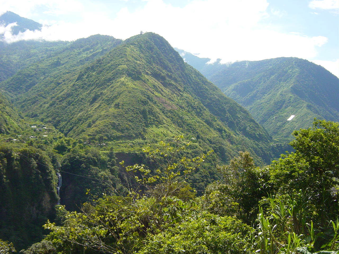 Lush green mountains with dense vegetation, a small waterfall in the distance, and a clear blue sky above.