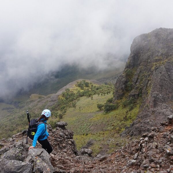 Two hikers standing on a rocky mountain trail looking towards a fog-covered peak.