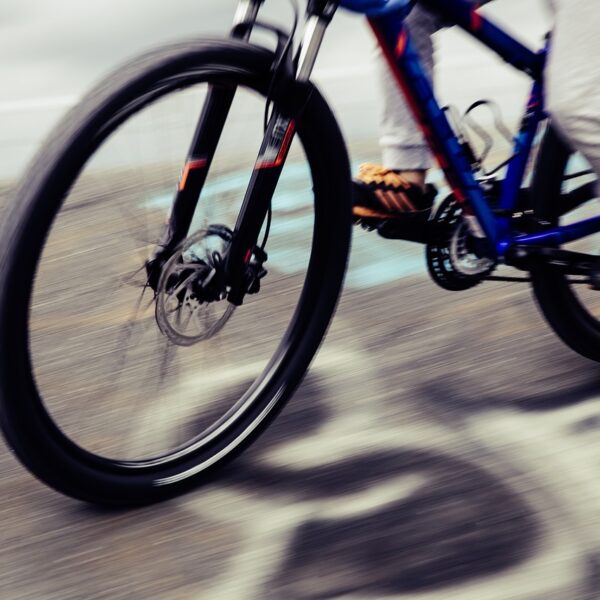 Motion-blurred image of a person cycling on a road, focusing on the spinning wheels of a blue bicycle.