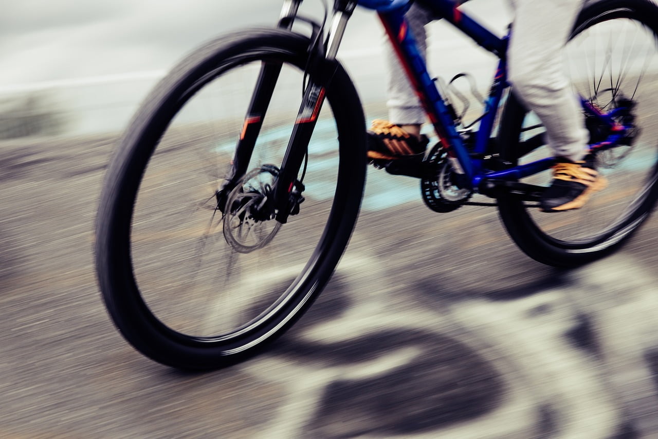 Motion-blurred image of a person cycling on a road, focusing on the spinning wheels of a blue bicycle.