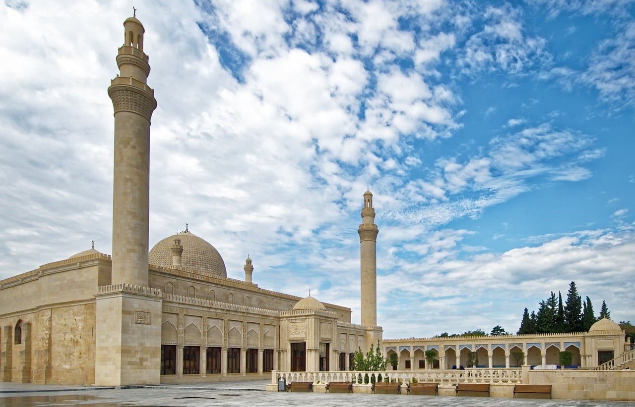 A grand mosque with a large dome and two tall minarets against a blue sky with scattered clouds.