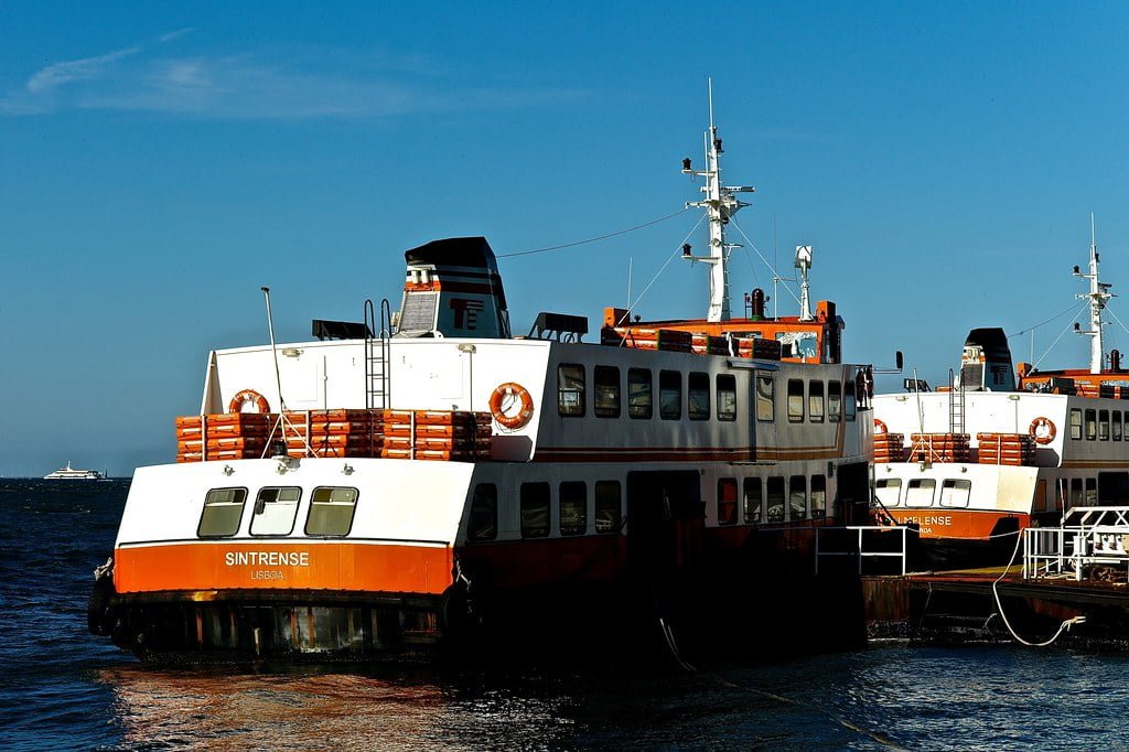 Two orange and white ferries docked at a port with clear blue sky in the background.