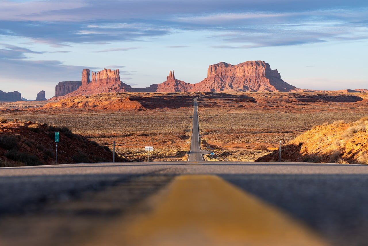 A straight road leading to Monument Valley, with the iconic sandstone buttes and mesas in the distance under a clear blue sky.