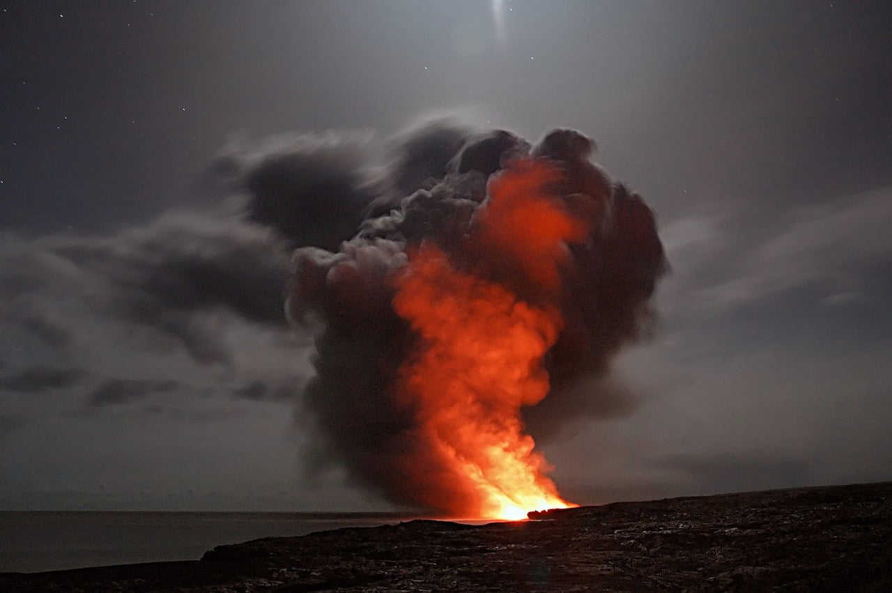 A volcanic eruption at night with red-hot lava illuminating smoke and ash clouds under a starry sky.