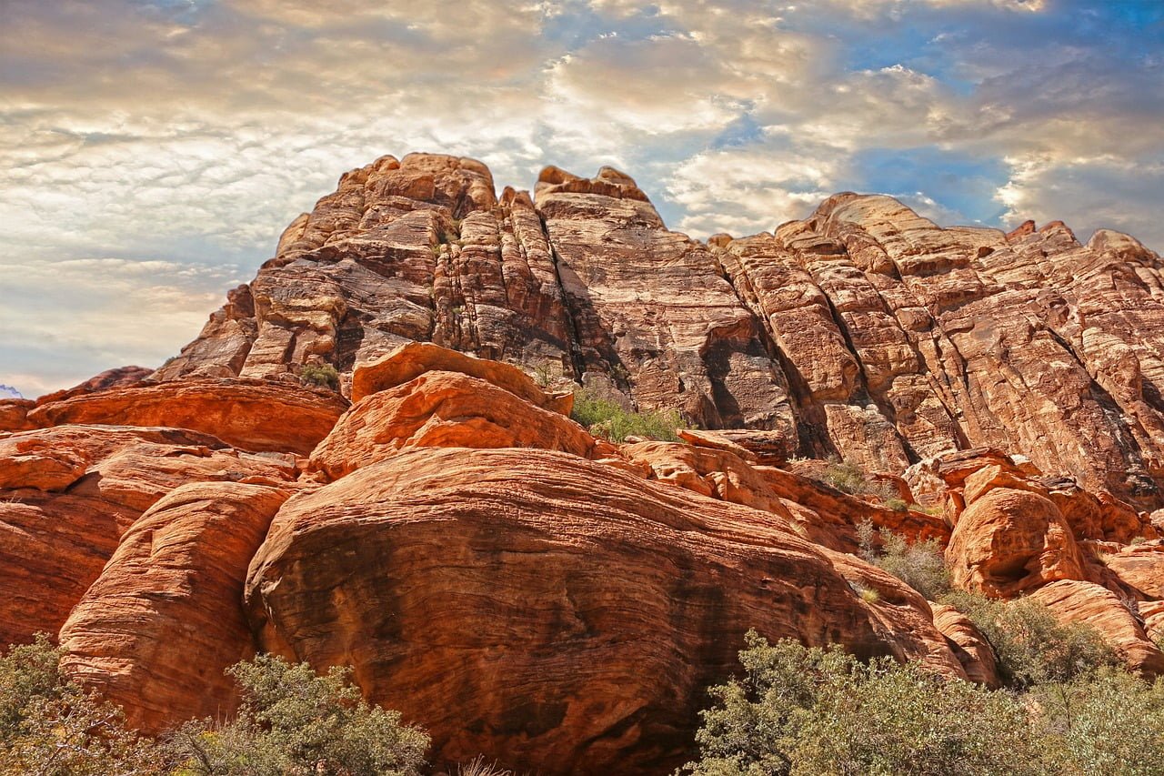 Red rock formations with striated patterns under a partly cloudy sky.
