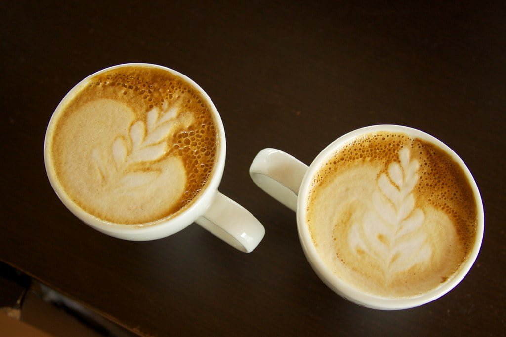 Two cups of cappuccino with latte art on a dark table.