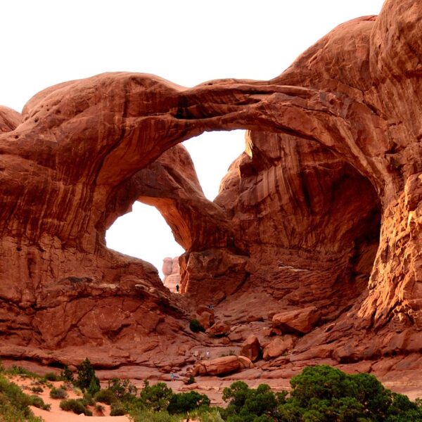 The Double Arch rock formation in Arches National Park, Utah, featuring two large arches interconnected within a massive red sandstone structure, with sparse vegetation in the foreground.
