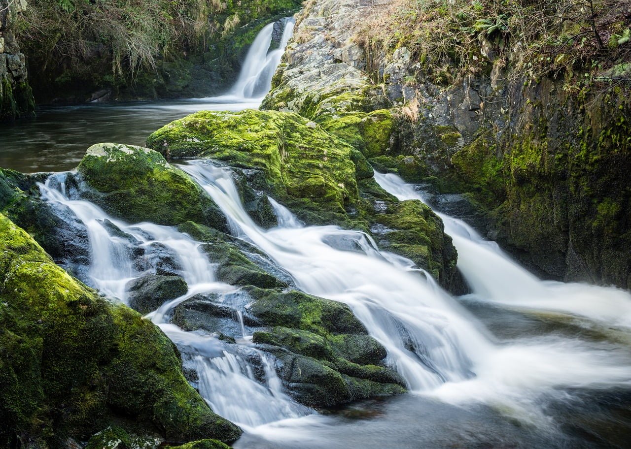 A serene waterfall cascading over moss-covered rocks into a tranquil pool.