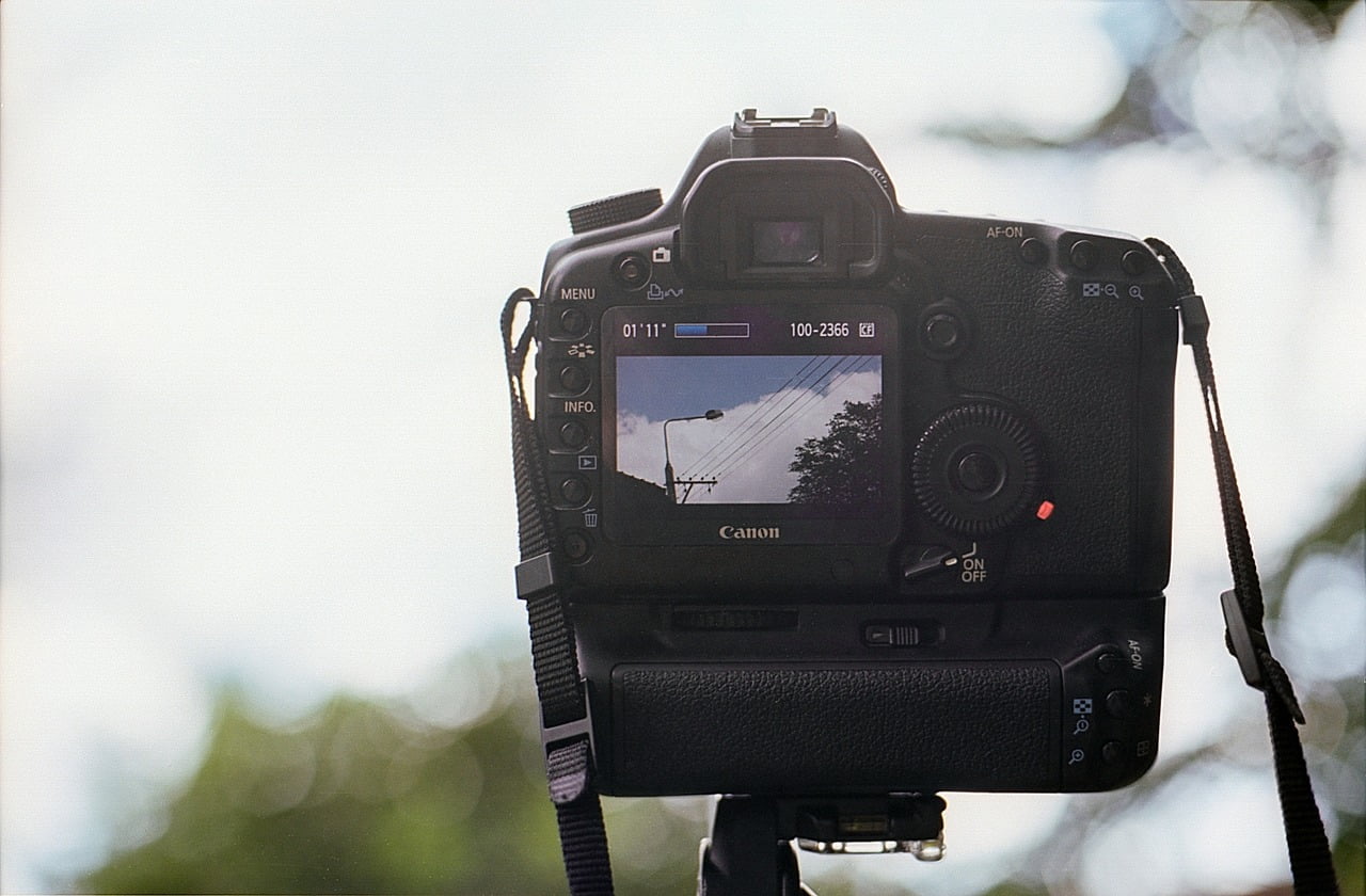 A DSLR camera with a displayed image on its screen showing a street light, power lines, and a partly cloudy sky.