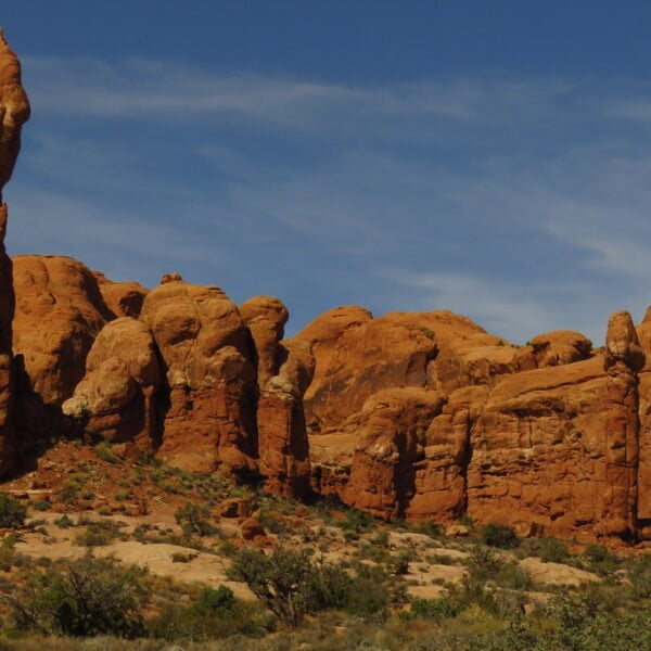 A towering red rock formation stands out amidst several large boulders under a blue sky with few clouds.