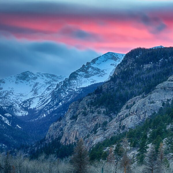 A serene mountain landscape at dusk with snow-capped peaks under a vibrant pink and blue sky.
