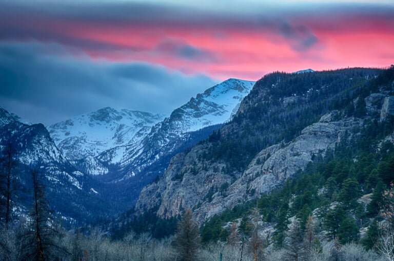 A serene mountain landscape at dusk with snow-capped peaks under a vibrant pink and blue sky.