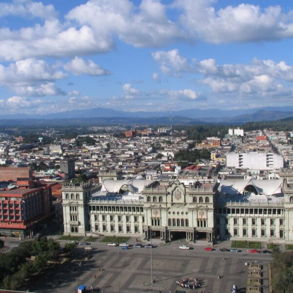 A panoramic view of a cityscape with an ornate building in the foreground and scattered clouds above.