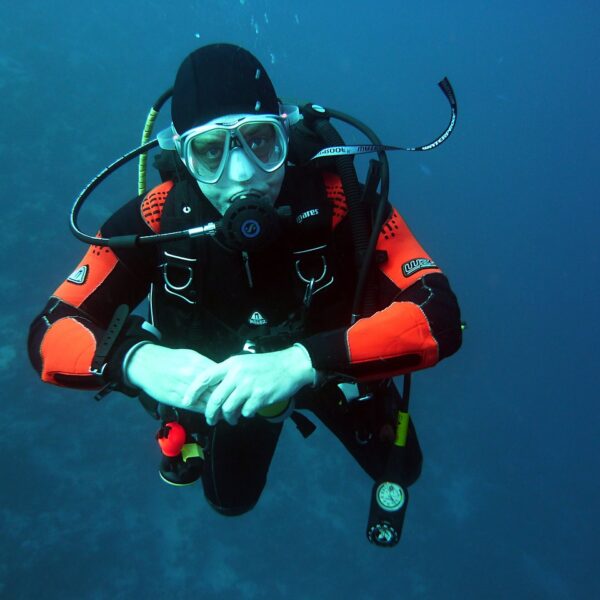 A scuba diver in black and red gear with a mask and regulator is neutrally buoyant underwater.