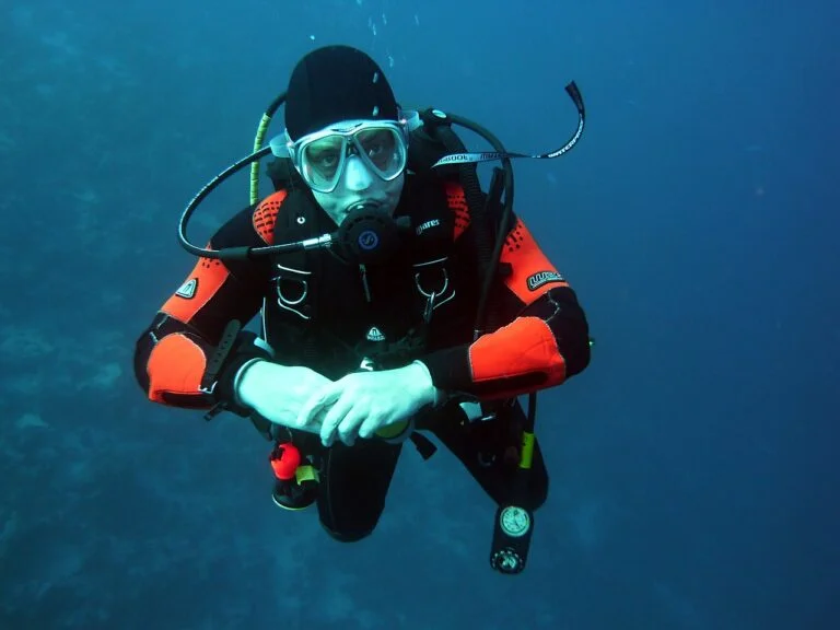 A scuba diver in black and red gear with a mask and regulator is neutrally buoyant underwater.