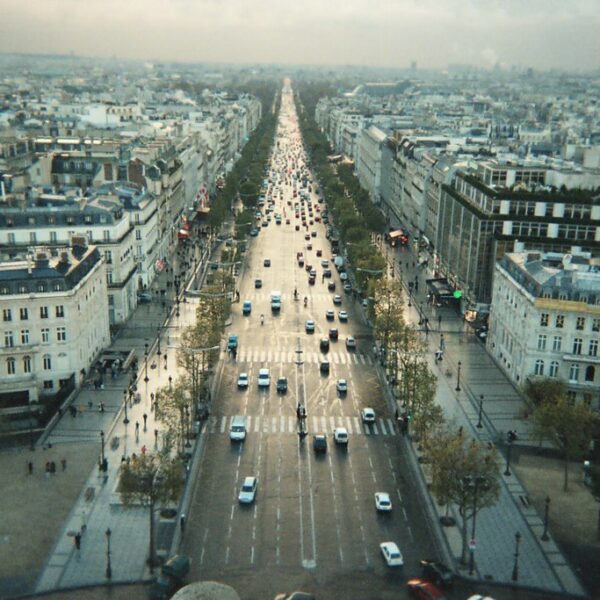 An aerial view of the Champs-Élysées in Paris, with traffic and classic Haussmann-style buildings lining the street, extending into the distance.