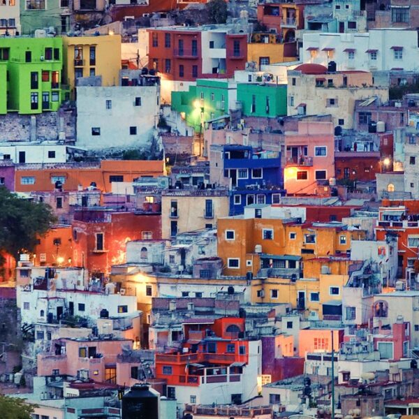 Colorful hillside houses densely packed in a stepped arrangement, displaying a variety of bright hues like green, yellow, red, and blue at dusk.