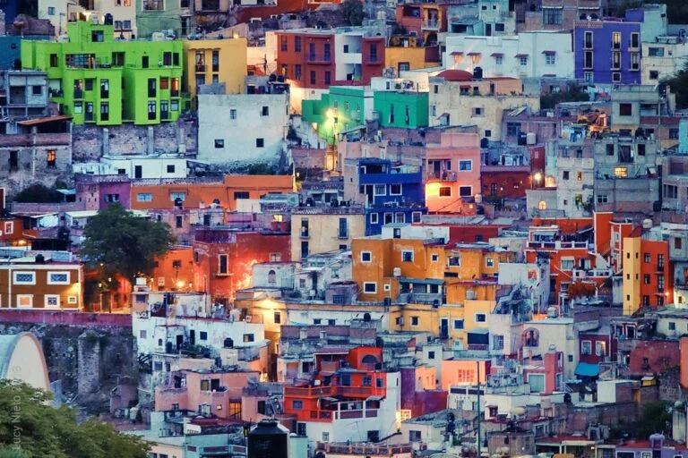Colorful hillside houses densely packed in a stepped arrangement, displaying a variety of bright hues like green, yellow, red, and blue at dusk.