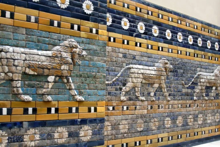 Ancient Mesopotamian lion relief tiles from the Ishtar Gate, showing a row of striding lions on a blue glazed brick wall with floral and geometric patterns.