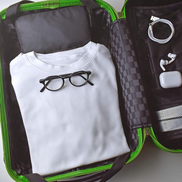 Open suitcase with neatly packed items including a folded white shirt, a pair of glasses, charging cable, and earphones in a black and green color scheme.