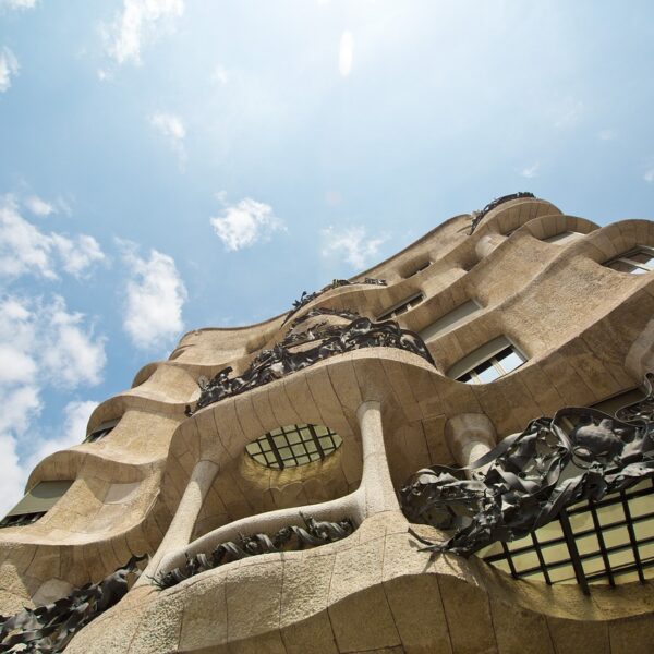 Exterior view of Casa MilĂ (La Pedrera) with its undulating stone facade and intricate wrought iron balconies against a blue sky with white clouds.