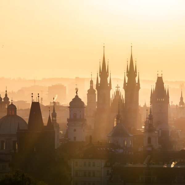 An aerial view of a city skyline at sunrise with silhouettes of historic buildings and spires against a golden sky.